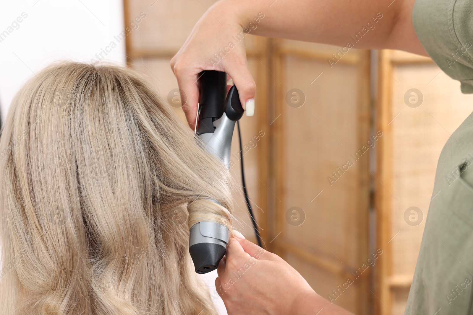 Hairdresser curling woman's hair in salon, closeup Photo of Hairdresser curling woman's hair in salon, closeup