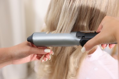 Photo of Hairdresser curling woman's hair in salon, closeup