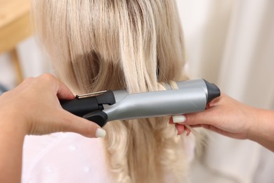 Photo of Hairdresser curling woman's hair in salon, closeup