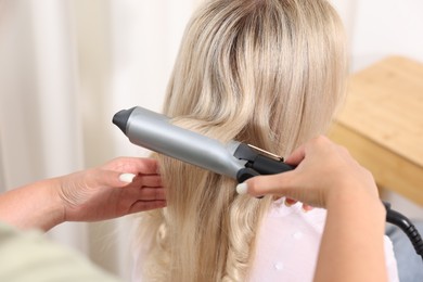 Photo of Hairdresser curling woman's hair in salon, closeup