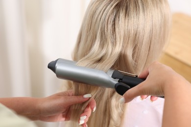 Photo of Hairdresser curling woman's hair in salon, closeup