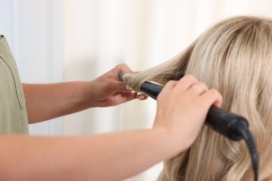 Photo of Hairdresser curling woman's hair in salon, closeup