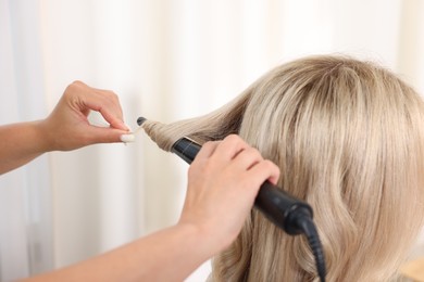 Photo of Hairdresser curling woman's hair in salon, closeup