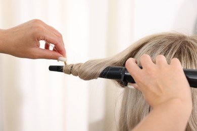 Photo of Hairdresser curling woman's hair in salon, closeup