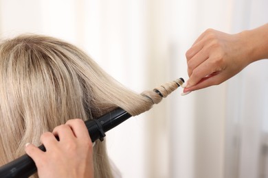 Photo of Hairdresser curling woman's hair in salon, closeup