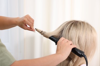 Photo of Hairdresser curling woman's hair in salon, closeup