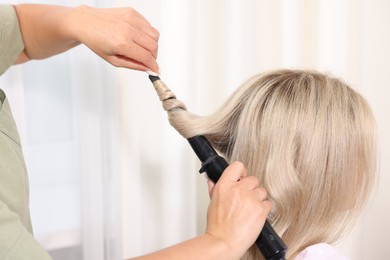 Photo of Hairdresser curling woman's hair in salon, closeup