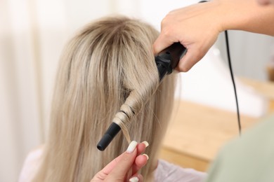 Photo of Hairdresser curling woman's hair in salon, closeup