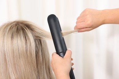 Photo of Hairdresser straightening woman's hair with flat iron in salon, closeup