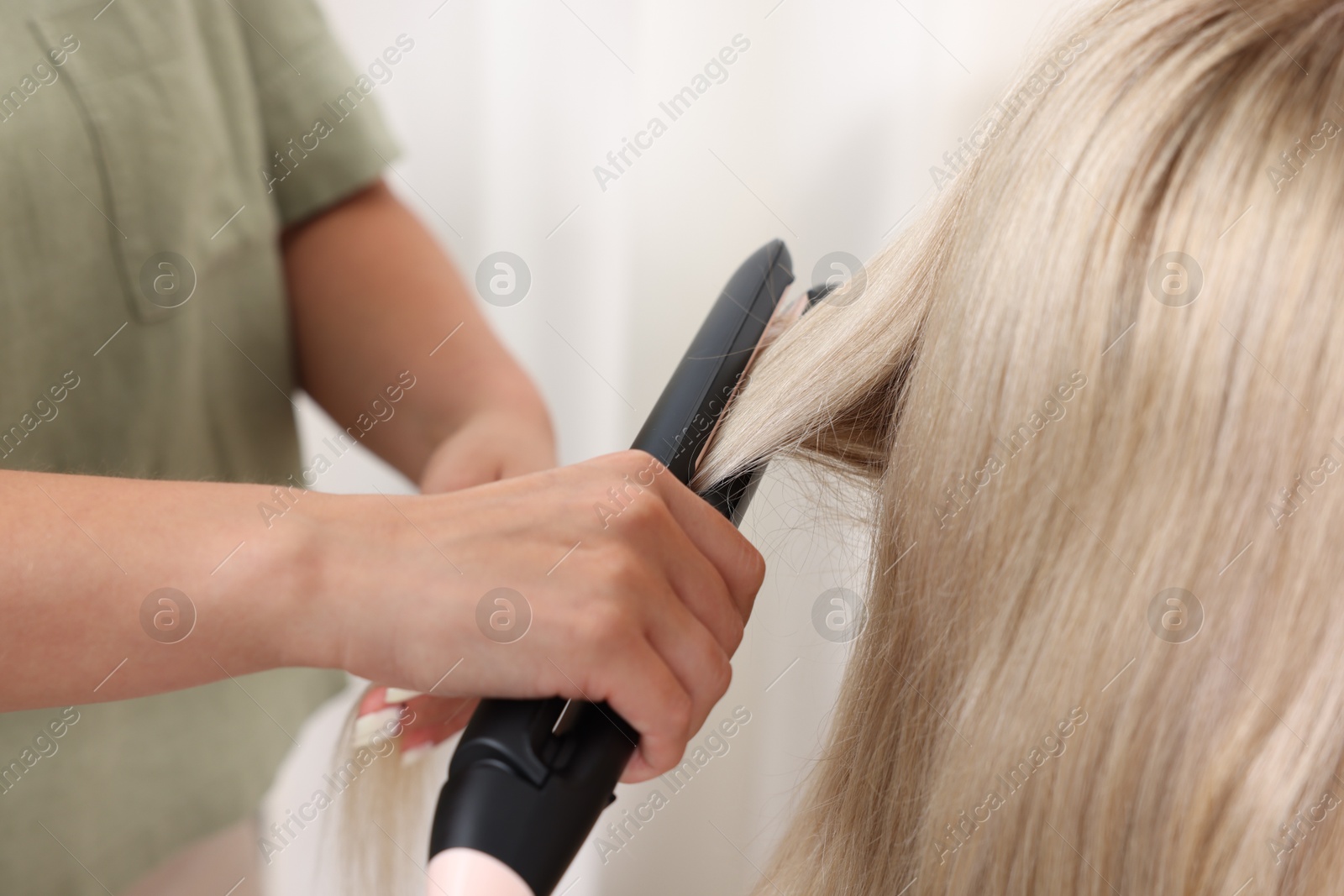 Hairdresser straightening woman's hair with flat iron in salon, closeup Photo of Hairdresser straightening woman's hair with flat iron in salon, closeup