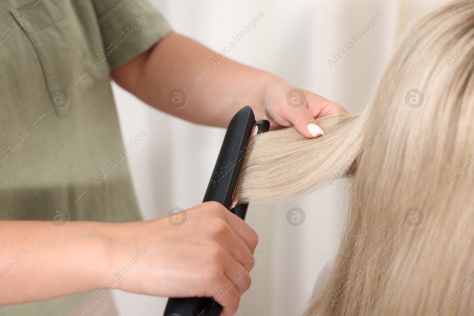 Hairdresser straightening woman's hair with flat iron in salon, closeup Photo of Hairdresser straightening woman's hair with flat iron in salon, closeup