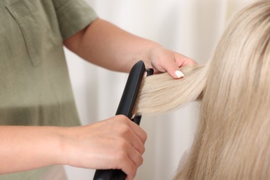 Photo of Hairdresser straightening woman's hair with flat iron in salon, closeup