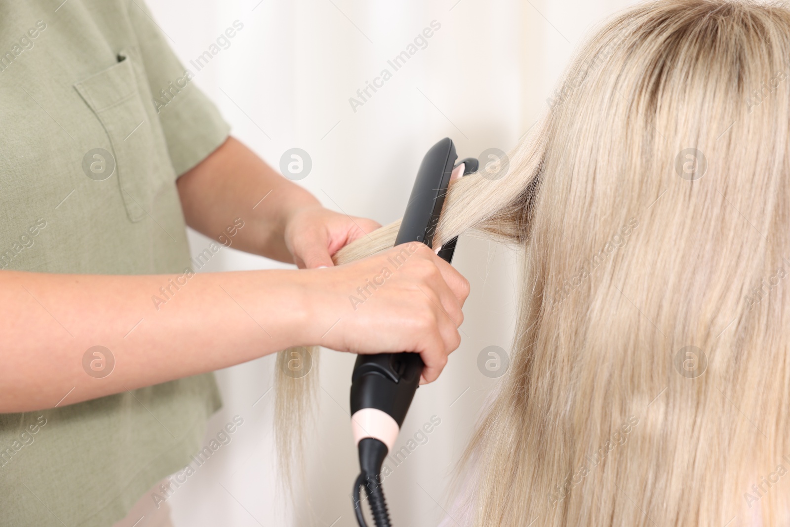 Hairdresser straightening woman's hair with flat iron in salon, closeup Photo of Hairdresser straightening woman's hair with flat iron in salon, closeup