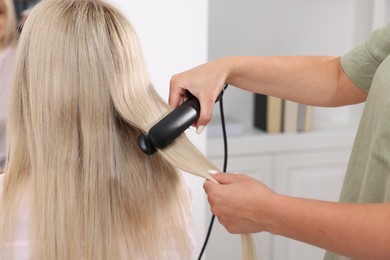 Photo of Hairdresser straightening woman's hair with flat iron in salon, closeup