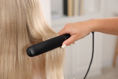 Photo of Hairdresser straightening woman's hair with flat iron in salon, closeup