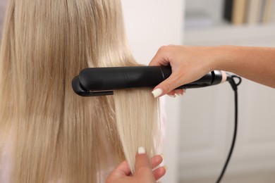 Photo of Hairdresser straightening woman's hair with flat iron in salon, closeup