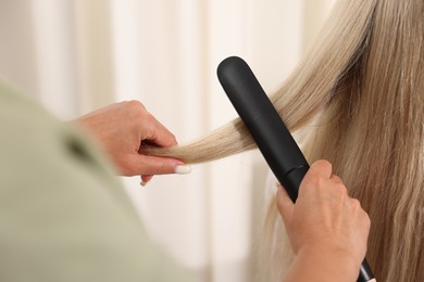 Photo of Hairdresser straightening woman's hair with flat iron in salon, closeup