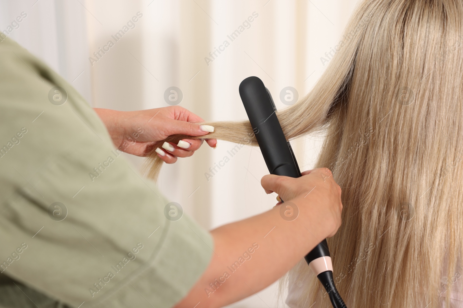 Hairdresser straightening woman's hair with flat iron in salon, closeup Photo of Hairdresser straightening woman's hair with flat iron in salon, closeup