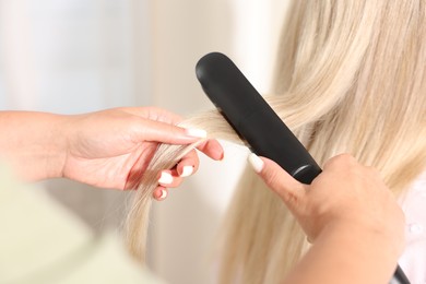 Photo of Hairdresser straightening woman's hair with flat iron in salon, closeup