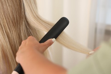 Photo of Hairdresser straightening woman's hair with flat iron in salon, closeup
