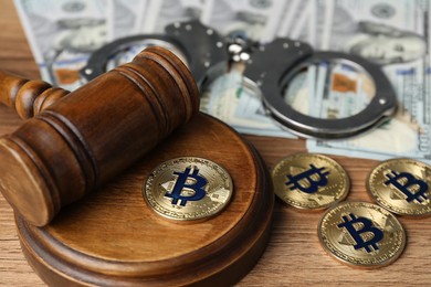 Photo of Cryptocurrency. Bitcoins, judge's gavel, handcuffs and dollars on wooden table, closeup