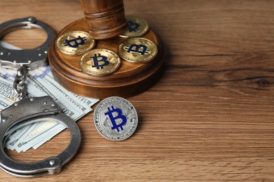 Photo of Cryptocurrency. Bitcoins, handcuffs, dollars and judge's gavel on wooden table, closeup. Space for text
