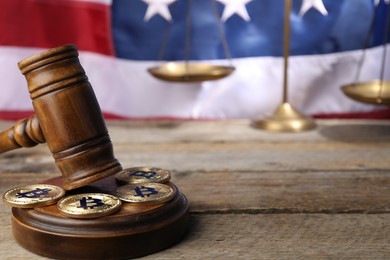 Photo of Cryptocurrency. Bitcoins, judge's gavel and scales on wooden table against American flag, closeup. Space for text
