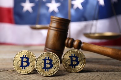 Photo of Cryptocurrency. Bitcoins, judge's gavel and scales on wooden table against American flag, closeup