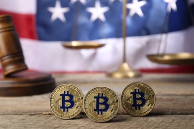 Photo of Cryptocurrency. Bitcoins, judge's gavel and scales on wooden table against American flag, closeup