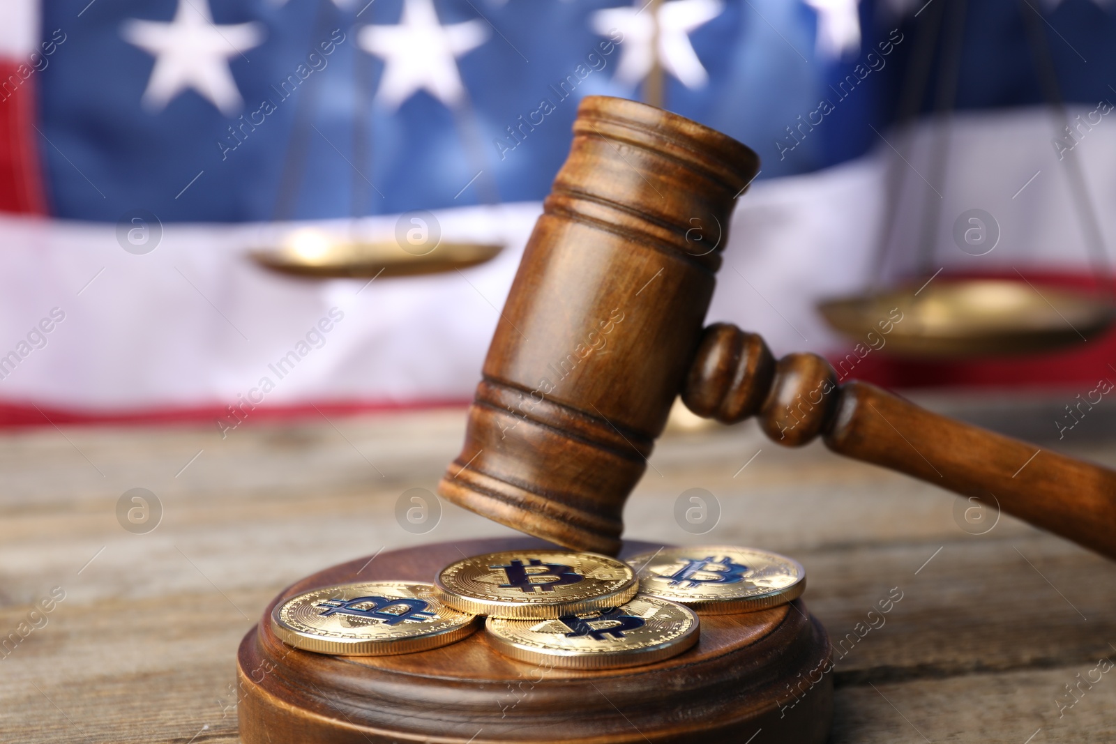 Photo of Cryptocurrency. Bitcoins, judge's gavel and scales on wooden table against American flag, closeup