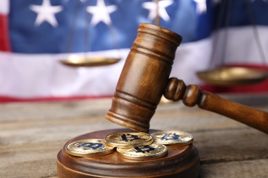 Photo of Cryptocurrency. Bitcoins, judge's gavel and scales on wooden table against American flag, closeup
