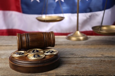 Photo of Cryptocurrency. Bitcoins, judge's gavel and scales on wooden table against American flag, closeup