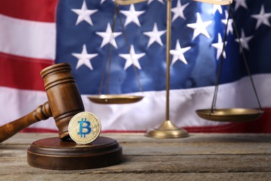 Photo of Cryptocurrency. Bitcoins, judge's gavel and scales on wooden table against American flag, closeup