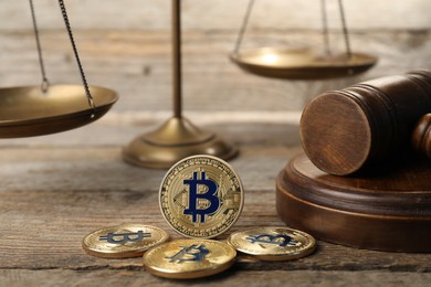 Photo of Cryptocurrency. Bitcoins, judge's gavel and scales on wooden table, closeup