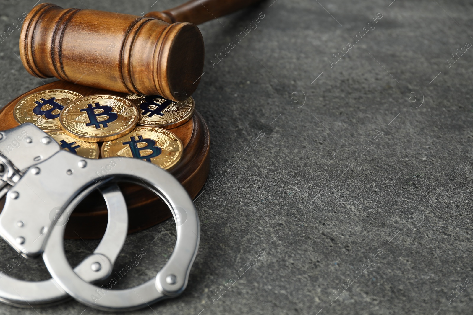 Photo of Cryptocurrency. Bitcoins, judge's gavel and handcuffs on grey table, closeup. Space for text