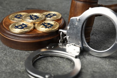 Photo of Cryptocurrency. Bitcoins, judge's gavel and handcuffs on grey table, closeup