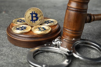 Photo of Cryptocurrency. Bitcoins, judge's gavel and handcuffs on grey table, closeup