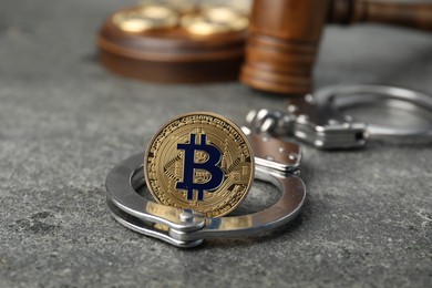 Photo of Cryptocurrency. Bitcoin, judge's gavel and handcuffs on grey table, closeup