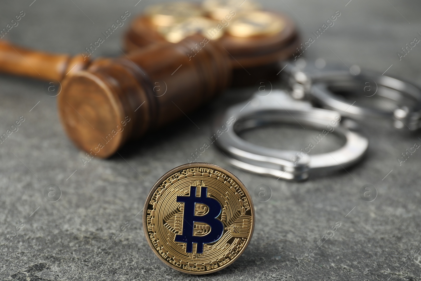 Photo of Cryptocurrency. Bitcoin, judge's gavel and handcuffs on grey table, closeup