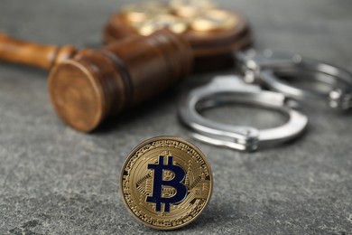 Photo of Cryptocurrency. Bitcoin, judge's gavel and handcuffs on grey table, closeup
