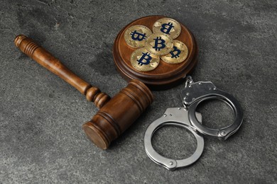 Photo of Cryptocurrency. Bitcoins, judge's gavel and handcuffs on grey table, above view