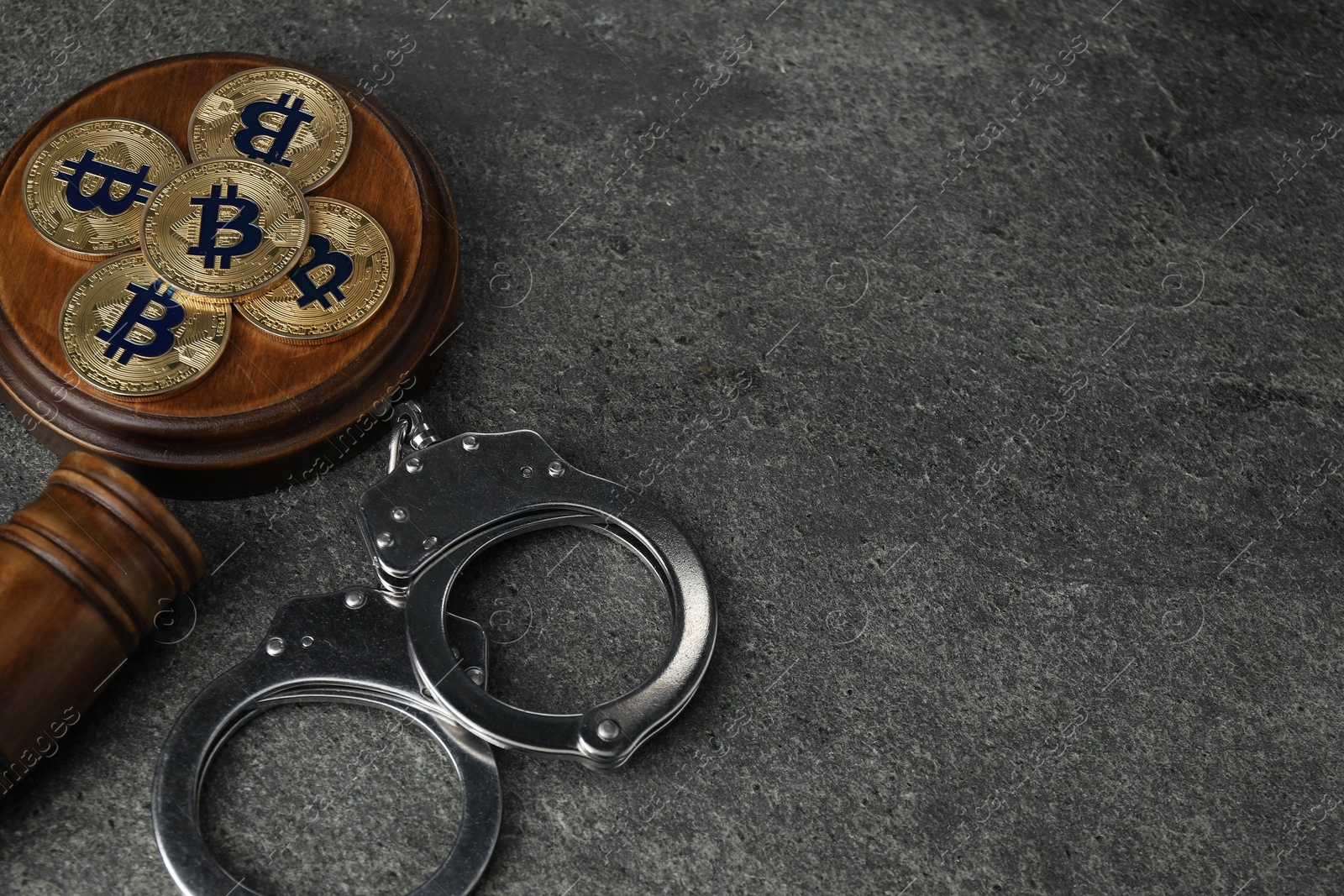 Photo of Cryptocurrency. Bitcoins, judge's gavel and handcuffs on grey table, above view. Space for text