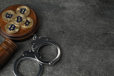 Photo of Cryptocurrency. Bitcoins, judge's gavel and handcuffs on grey table, above view. Space for text
