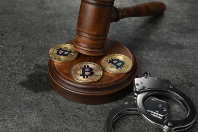 Photo of Cryptocurrency. Bitcoins, judge's gavel and handcuffs on grey table, closeup