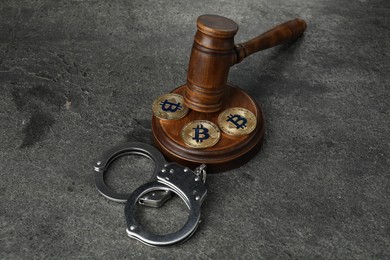 Photo of Cryptocurrency. Bitcoins, judge's gavel and handcuffs on grey table
