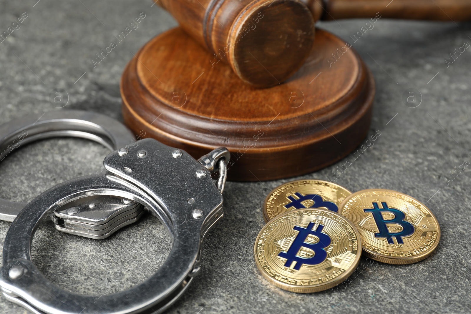 Photo of Cryptocurrency. Bitcoins, judge's gavel and handcuffs on grey table, closeup
