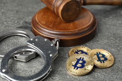 Photo of Cryptocurrency. Bitcoins, judge's gavel and handcuffs on grey table, closeup