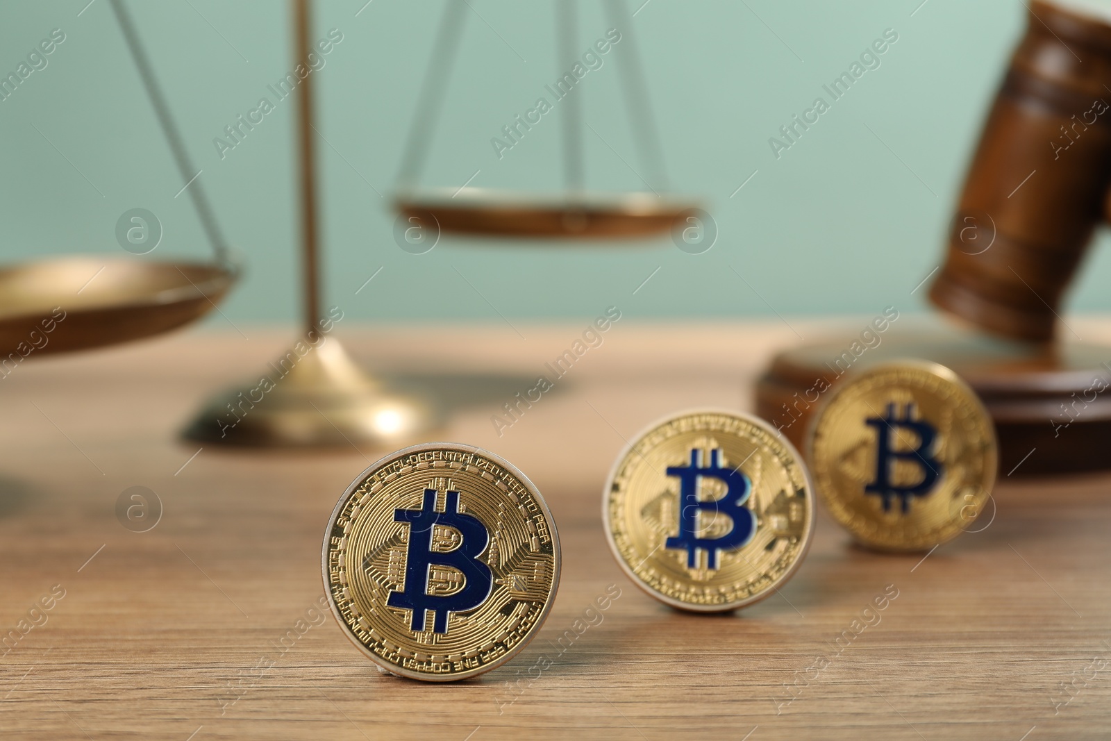 Photo of Cryptocurrency. Bitcoins, judge's gavel and scales on wooden table, closeup