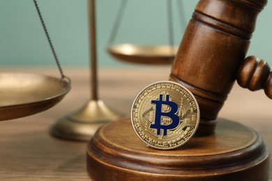 Photo of Cryptocurrency. Bitcoin, judge's gavel and scales on wooden table, closeup