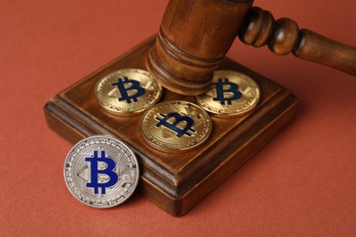 Photo of Cryptocurrency. Bitcoins and judge's gavel on red-brown background, closeup